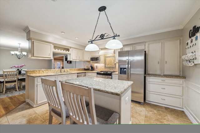 kitchen featuring appliances with stainless steel finishes, ornamental molding, pendant lighting, a chandelier, and a center island