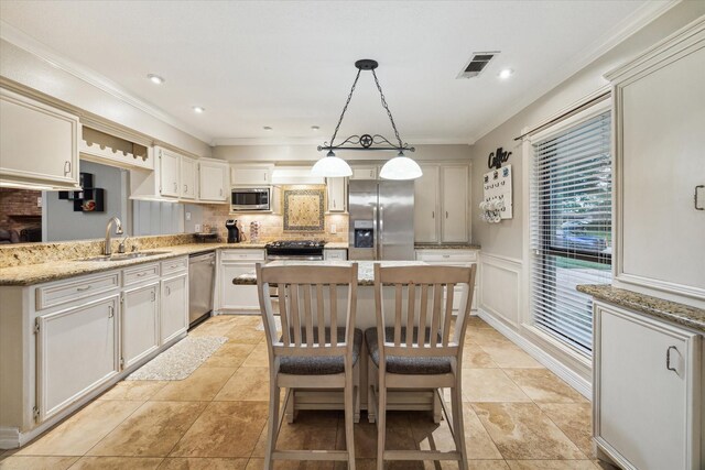 kitchen featuring stainless steel appliances, a sink, ornamental molding, backsplash, and a kitchen island