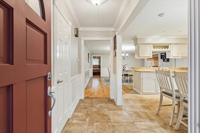 entryway featuring crown molding, wainscoting, a decorative wall, and light tile patterned floors