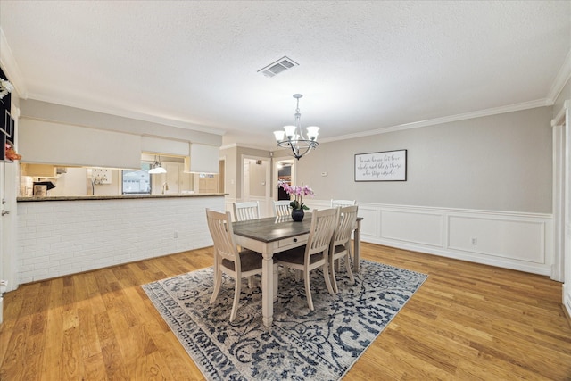 dining area with a chandelier, ornamental molding, a wainscoted wall, a textured ceiling, and light wood-style flooring