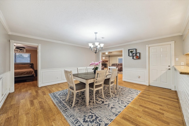 dining area with a chandelier, light wood-style floors, crown molding, a wainscoted wall, and a textured ceiling