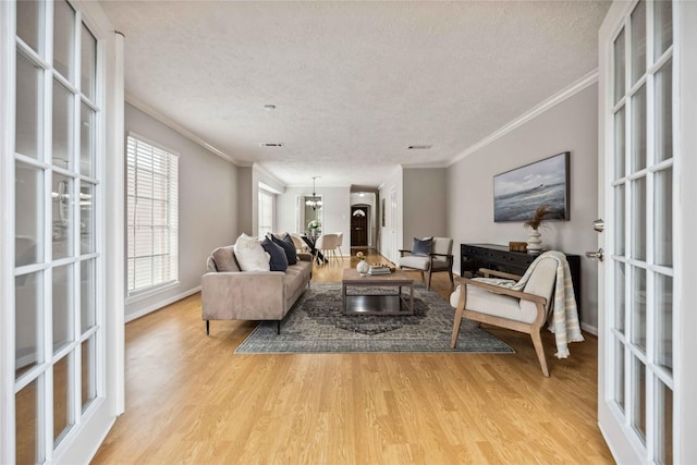 living area with light wood-type flooring, a textured ceiling, crown molding, baseboards, and french doors