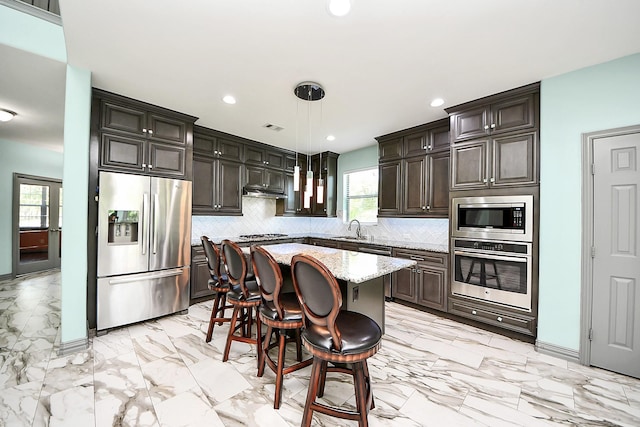 kitchen featuring stainless steel appliances, tasteful backsplash, a sink, light marble finish floors, and pendant lighting