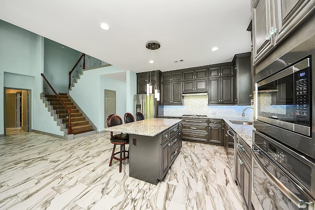 kitchen with appliances with stainless steel finishes, a breakfast bar area, tasteful backsplash, a sink, and light stone counters