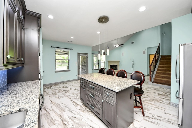 kitchen with freestanding refrigerator, a breakfast bar area, a ceiling fan, recessed lighting, and light marble finish floors