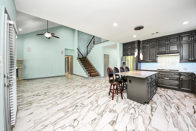 kitchen with stainless steel appliances, a breakfast bar area, ceiling fan, decorative backsplash, and light stone countertops