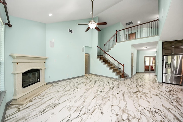 unfurnished living room featuring high vaulted ceiling, ceiling fan, a glass covered fireplace, stairway, and baseboards