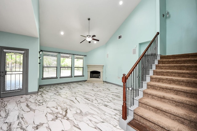 unfurnished living room with a ceiling fan, a fireplace, stairway, baseboards, and high vaulted ceiling