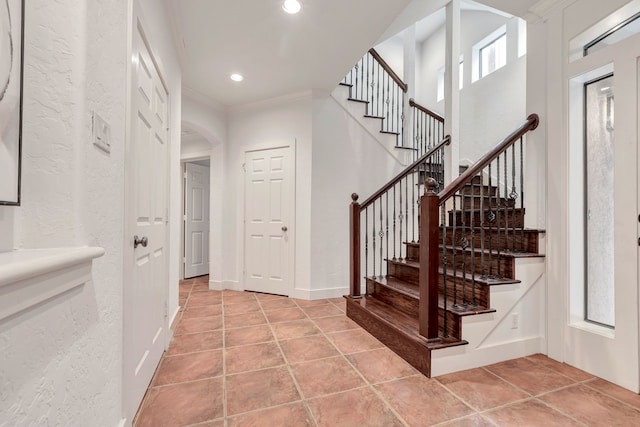 staircase featuring ornamental molding, arched walkways, recessed lighting, a textured wall, and tile patterned floors