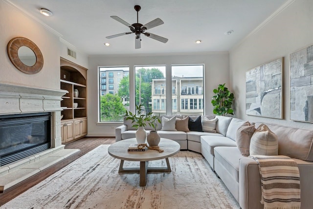 living area with ornamental molding, wood finished floors, ceiling fan, a high end fireplace, and recessed lighting