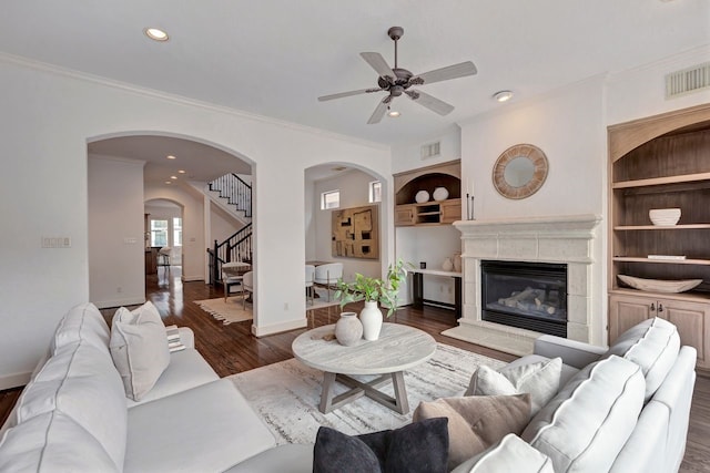 living area featuring ceiling fan, wood finished floors, arched walkways, stairway, and built in features