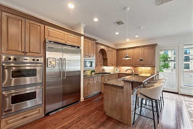 kitchen featuring built in appliances, ornamental molding, dark stone countertops, a sink, and decorative backsplash