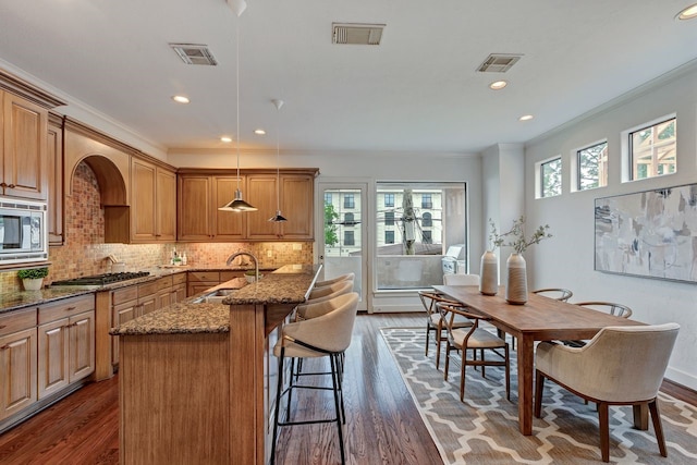 kitchen featuring a sink, appliances with stainless steel finishes, crown molding, dark wood-style flooring, and dark stone counters
