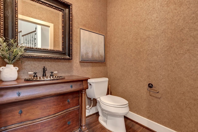 half bathroom with baseboards, wood finished floors, toilet, and vanity