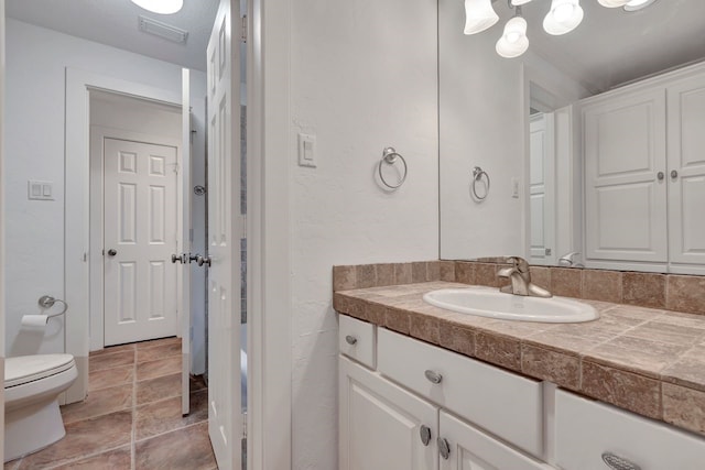 bathroom with toilet, vanity, and a textured wall