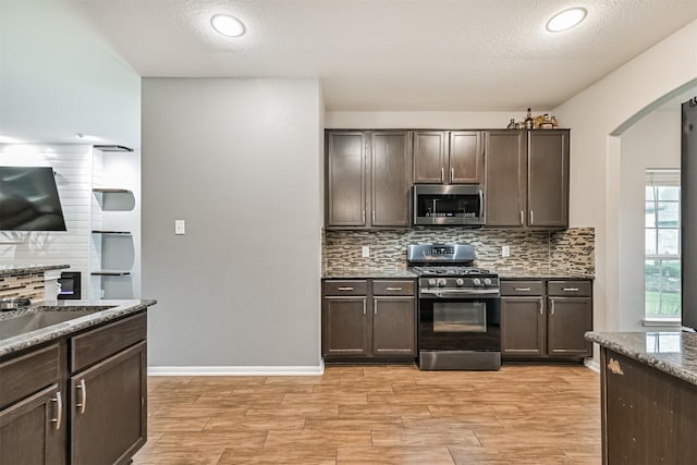 12750 Tullich Ln, Humble, TX 77346 - kitchen featuring appliances with stainless steel finishes, arched walkways, dark brown cabinetry, tasteful backsplash, and a textured ceiling