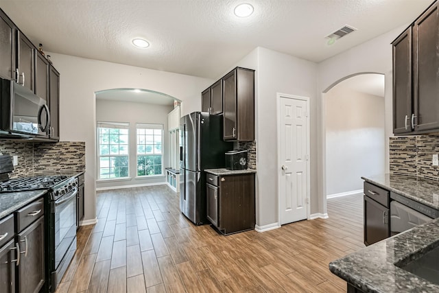 12750 Tullich Ln, Humble, TX 77346 - kitchen featuring appliances with stainless steel finishes, arched walkways, dark stone counters, dark brown cabinets, and a textured ceiling