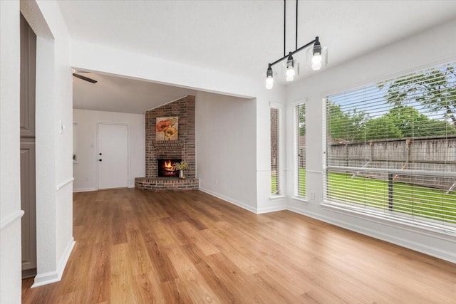 unfurnished dining area with light wood finished floors, a fireplace, ceiling fan, baseboards, and vaulted ceiling