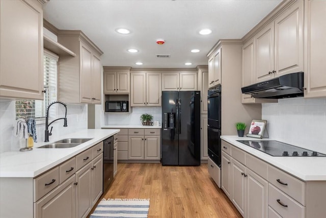 kitchen with black appliances, under cabinet range hood, a sink, backsplash, and recessed lighting