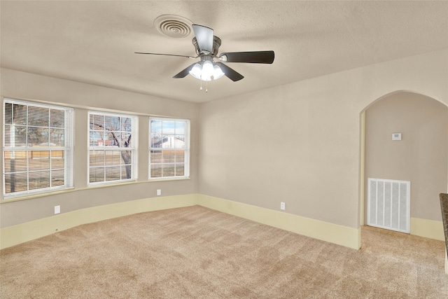 unfurnished room featuring carpet flooring, arched walkways, ceiling fan, and a textured ceiling