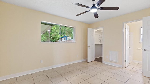 unfurnished bedroom with light tile patterned floors, baseboards, a walk in closet, a closet, and a ceiling fan