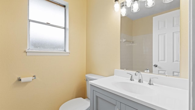 bathroom with toilet, a shower, vanity, and a textured wall