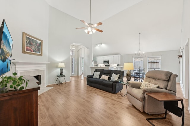 living area with arched walkways, high vaulted ceiling, ceiling fan, light wood finished floors, and a chandelier