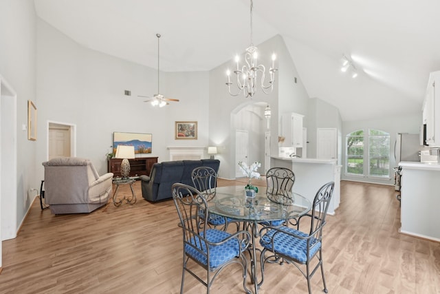 dining space featuring high vaulted ceiling, a ceiling fan, light wood finished floors, a chandelier, and arched walkways