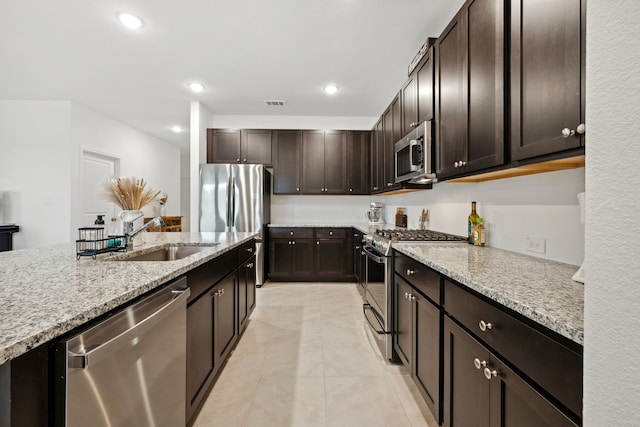 kitchen with stainless steel appliances, a sink, light stone countertops, dark brown cabinetry, and recessed lighting
