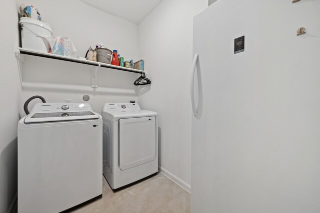 washroom featuring washer and dryer, light tile patterned floors, and baseboards