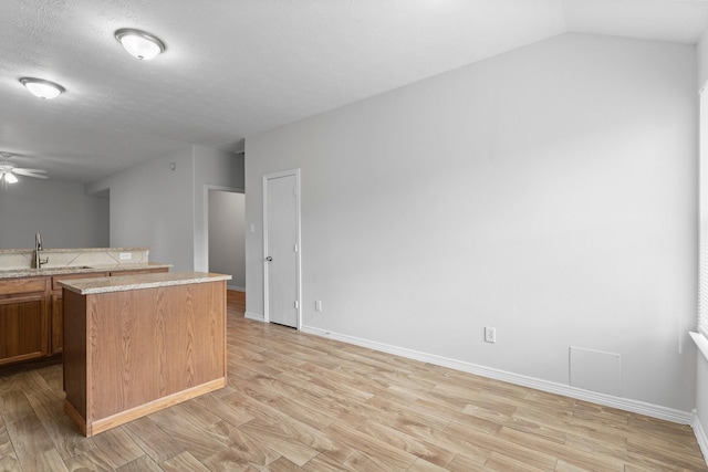 kitchen featuring a sink, light wood-type flooring, a ceiling fan, a kitchen island, and baseboards