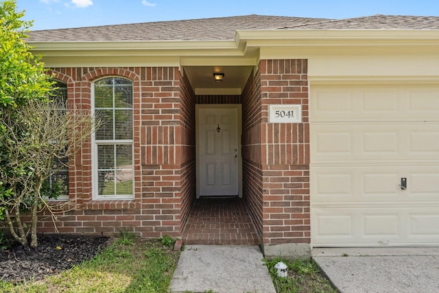 property entrance with brick siding, roof with shingles, and an attached garage