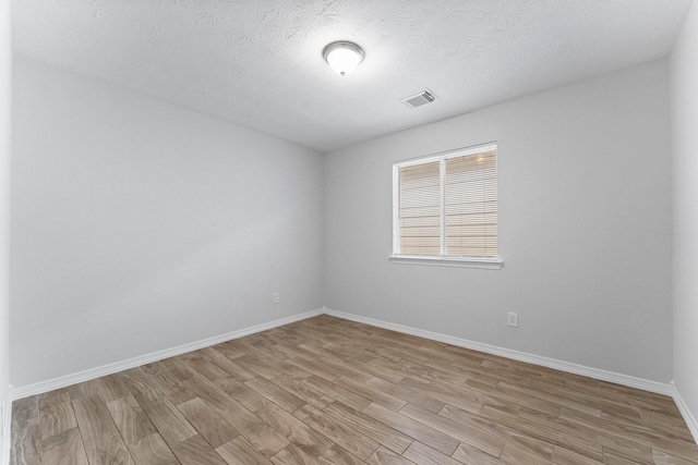 unfurnished room featuring light wood finished floors, baseboards, and a textured ceiling
