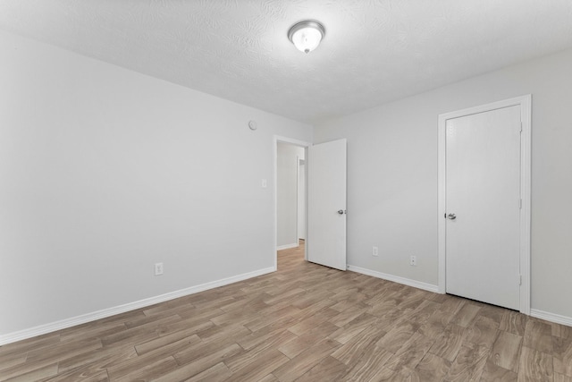 unfurnished bedroom featuring light wood finished floors, baseboards, and a textured ceiling