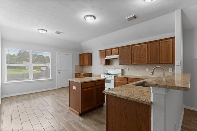 kitchen with a sink, under cabinet range hood, white gas range oven, baseboards, and decorative backsplash