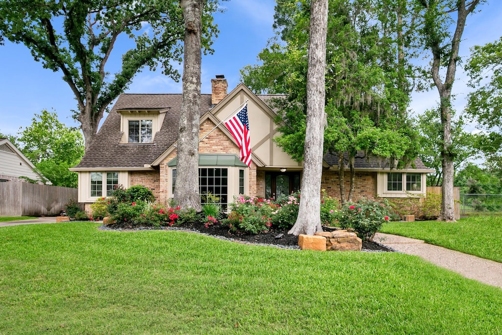 tudor house with a chimney, brick siding, and roof with shingles