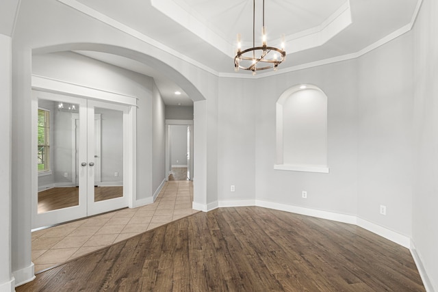 spare room with arched walkways, wood finished floors, ornamental molding, a chandelier, and french doors