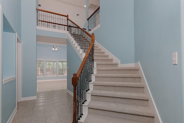 stairway with a towering ceiling, a ceiling fan, baseboards, and tile patterned floors