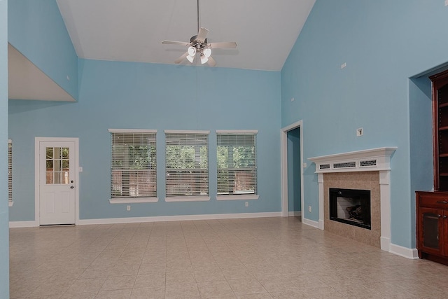 unfurnished living room featuring high vaulted ceiling, ceiling fan, plenty of natural light, a tiled fireplace, and baseboards