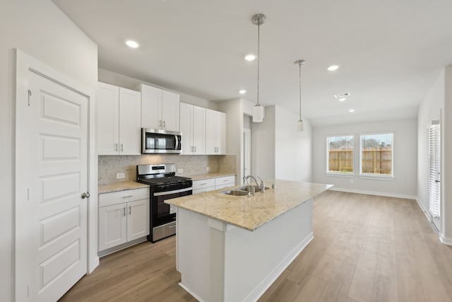 kitchen with appliances with stainless steel finishes, a sink, backsplash, light wood finished floors, and an island with sink