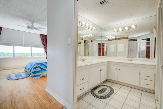 full bath with a textured ceiling, double vanity, a ceiling fan, connected bathroom, and baseboards