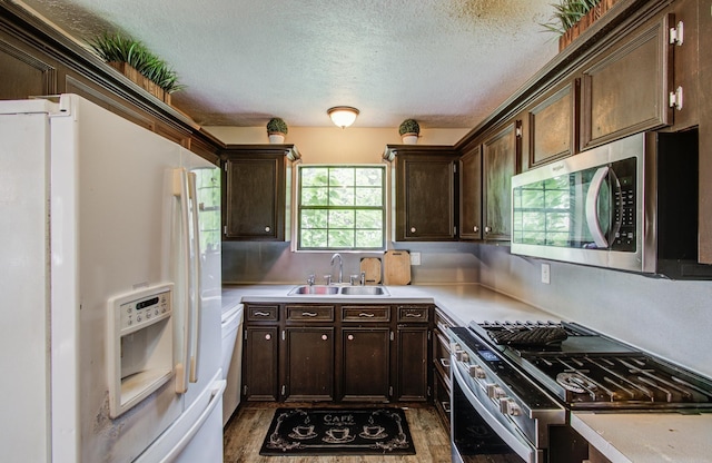 2915 Quailwood St, Houston, TX 77014 - kitchen with stainless steel appliances, a sink, a textured ceiling, dark brown cabinets, and light countertops