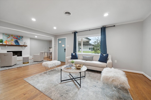 living room featuring wood finished floors, crown molding, recessed lighting, a fireplace, and baseboards