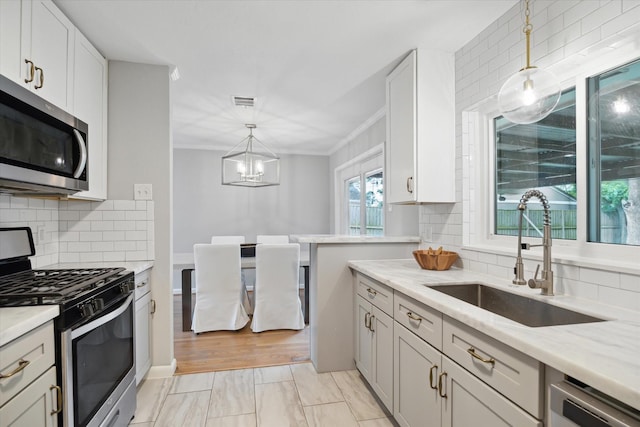 kitchen featuring stainless steel appliances, a sink, a chandelier, backsplash, and crown molding