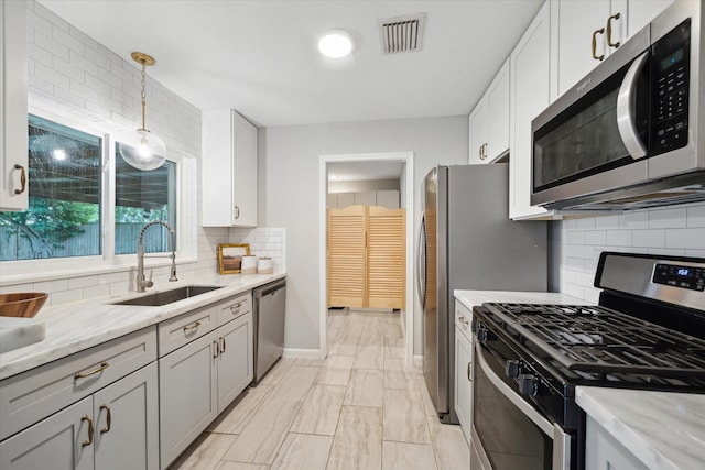 kitchen featuring appliances with stainless steel finishes, a sink, tasteful backsplash, decorative light fixtures, and light stone counters