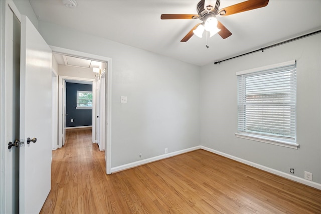 unfurnished room with attic access, light wood-style floors, a ceiling fan, and baseboards
