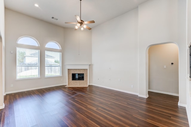 8246 Mandalay Bay Dr, Baytown, TX 77523 - unfurnished living room with arched walkways, a ceiling fan, dark wood-style flooring, a towering ceiling, and a tiled fireplace