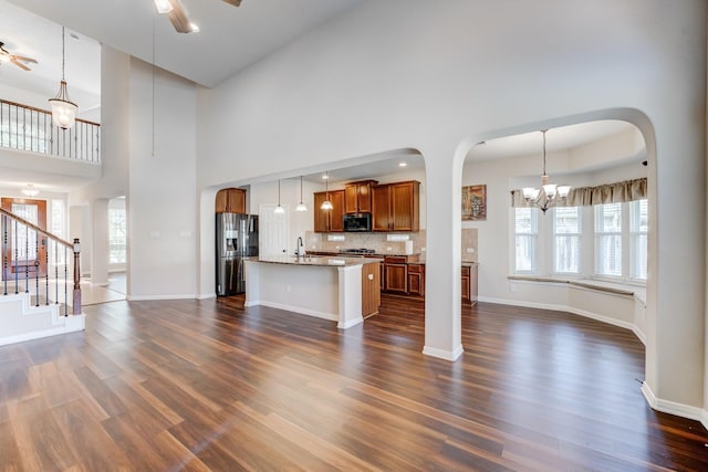 8246 Mandalay Bay Dr, Baytown, TX 77523 - unfurnished living room with ceiling fan, a chandelier, arched walkways, dark wood-style flooring, and a high ceiling