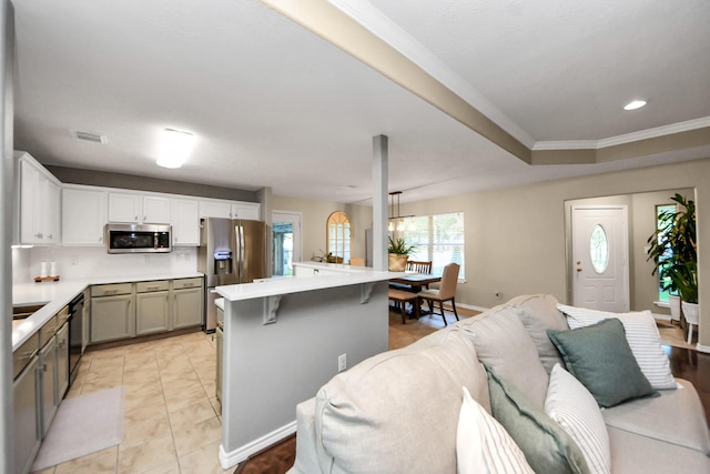 kitchen with stainless steel appliances, light countertops, a center island, a kitchen bar, and crown molding