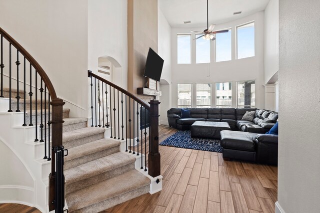 staircase with a high ceiling, wood finished floors, ceiling fan, and baseboards